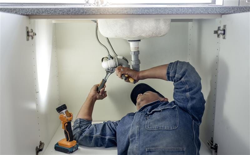 Plumber repairing pipes beneath a bathroom sink in Powder Springs