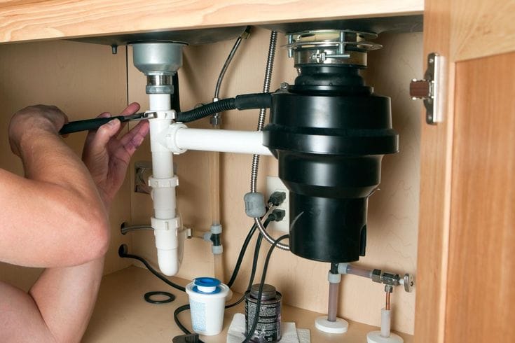 Plumber installing a garbage disposal beneath a kitchen sink in Powder Springs