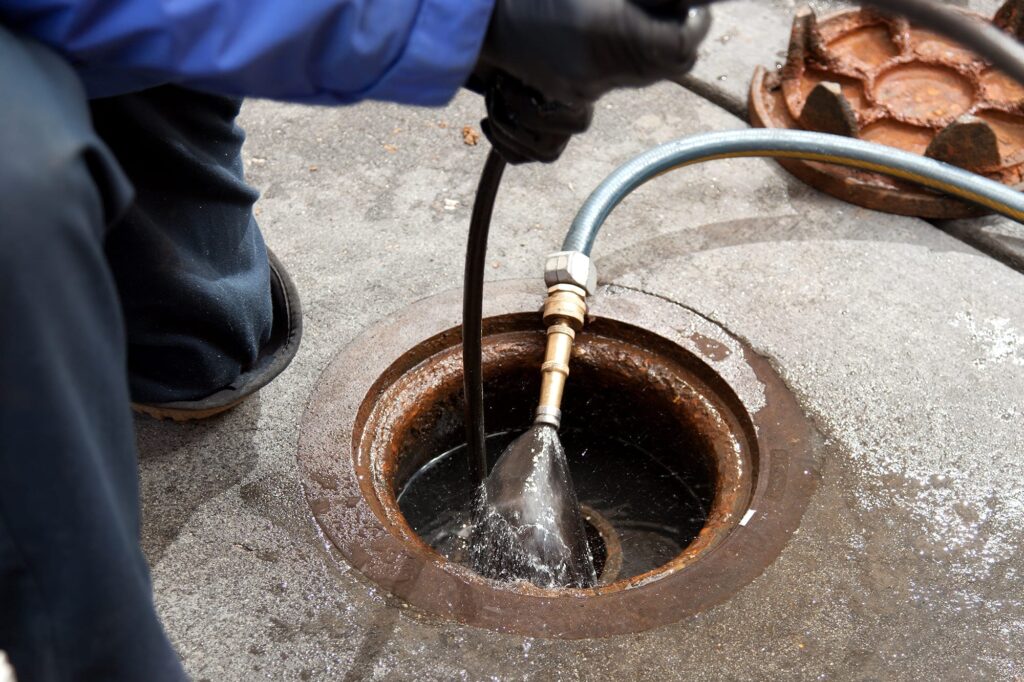 Plumber hydro jetting a sewer line through a manhole in Powder Springs