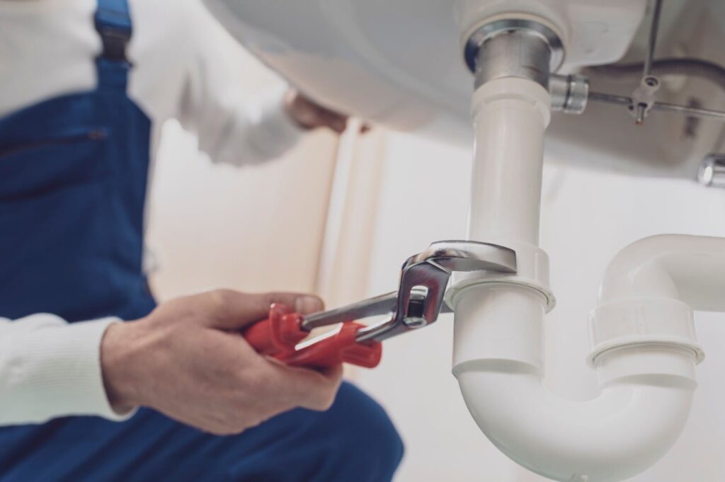 Plumber repairing a white drain pipe beneath a sink in Powder Springs