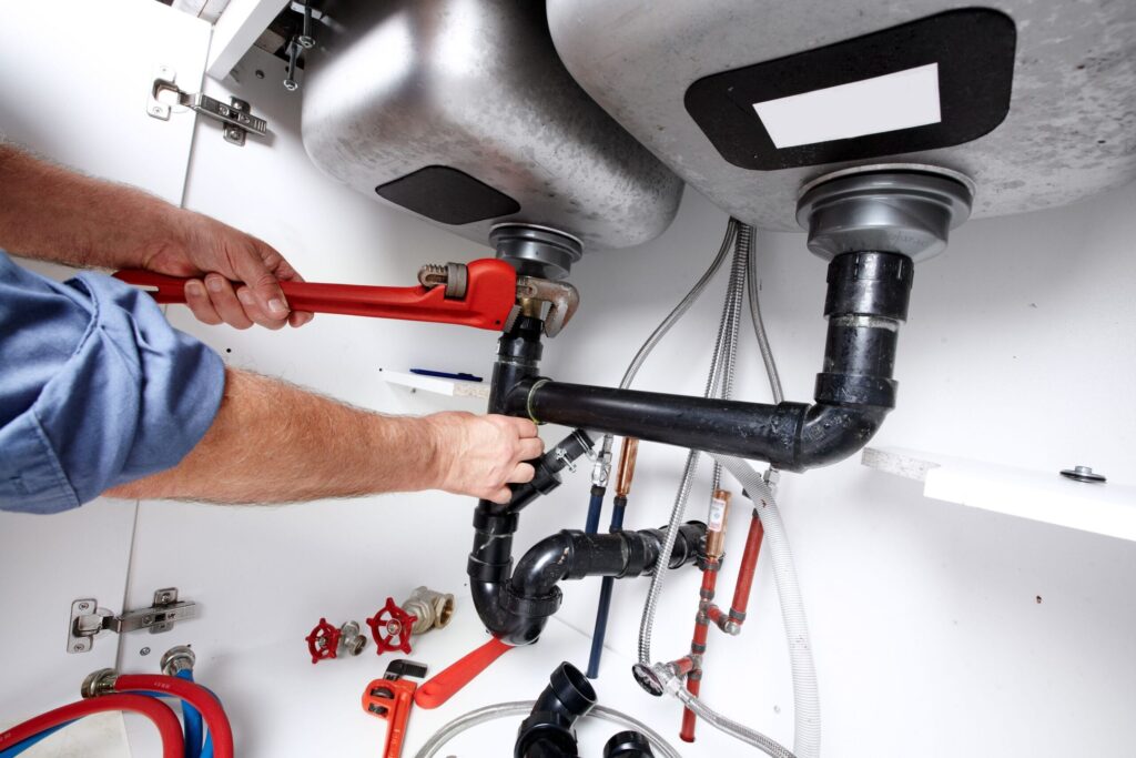 Plumber repairing drain pipes beneath a kitchen sink in Powder Springs